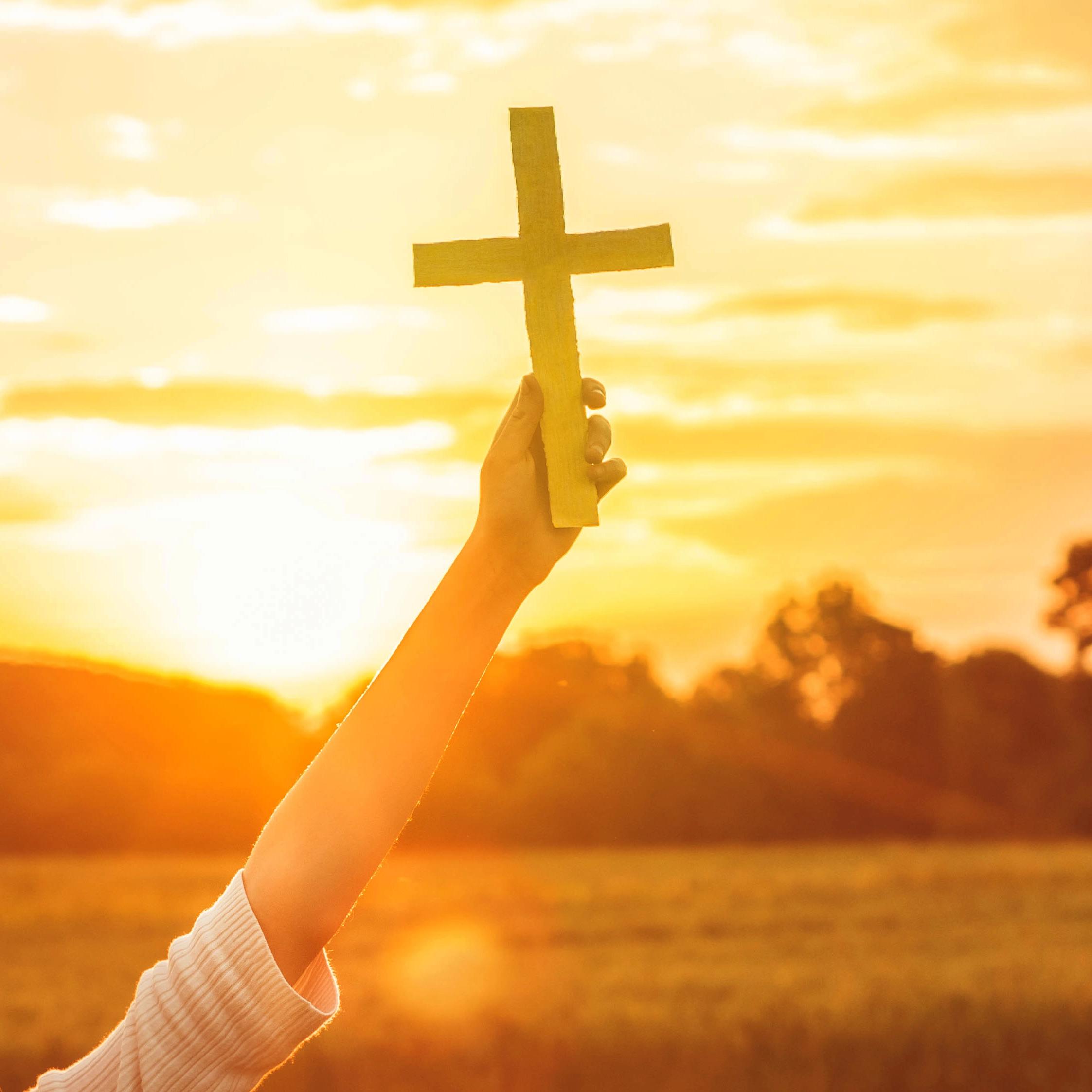 hand holding a cross during sunset
