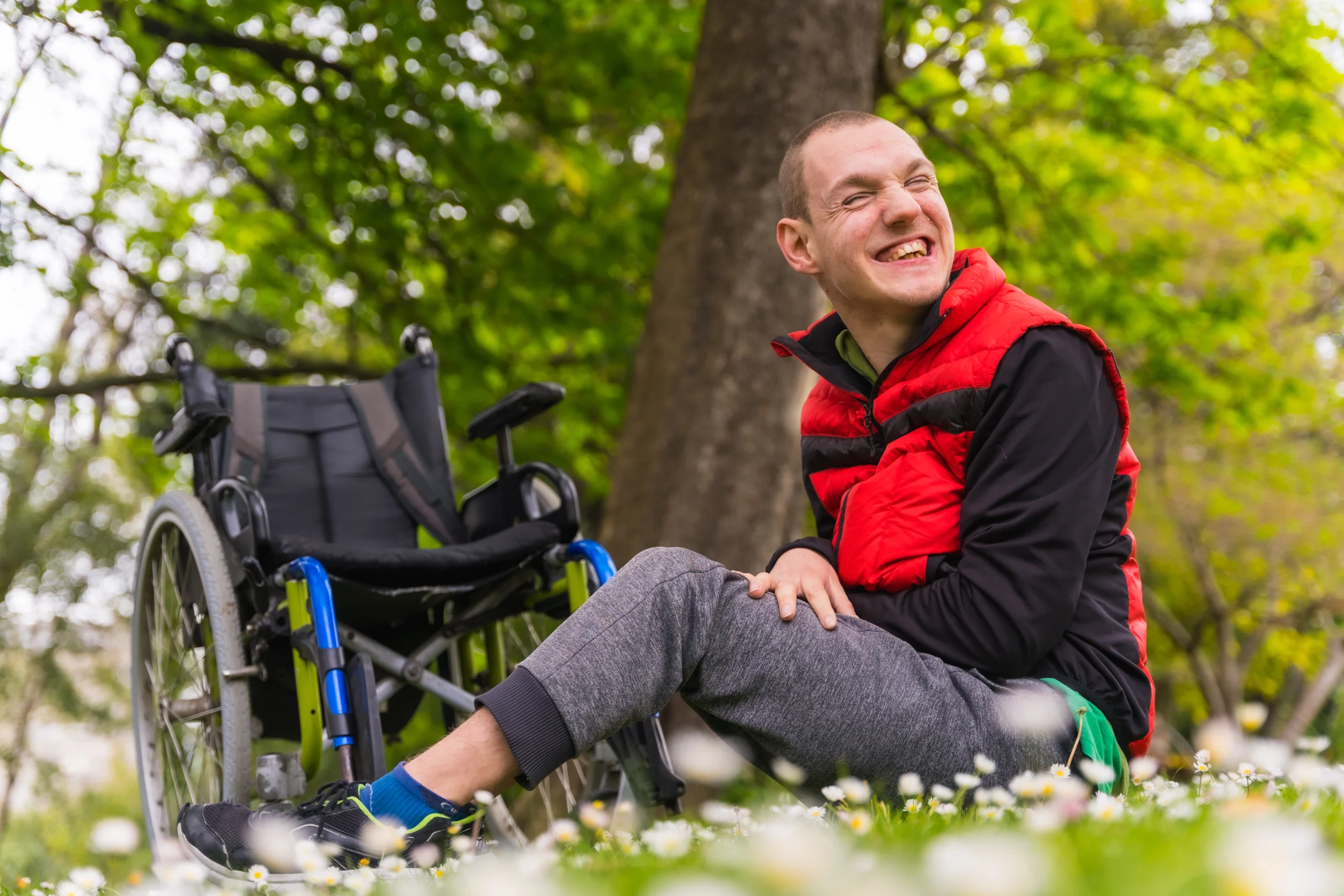 young disabled guy sitting outside smiling. 