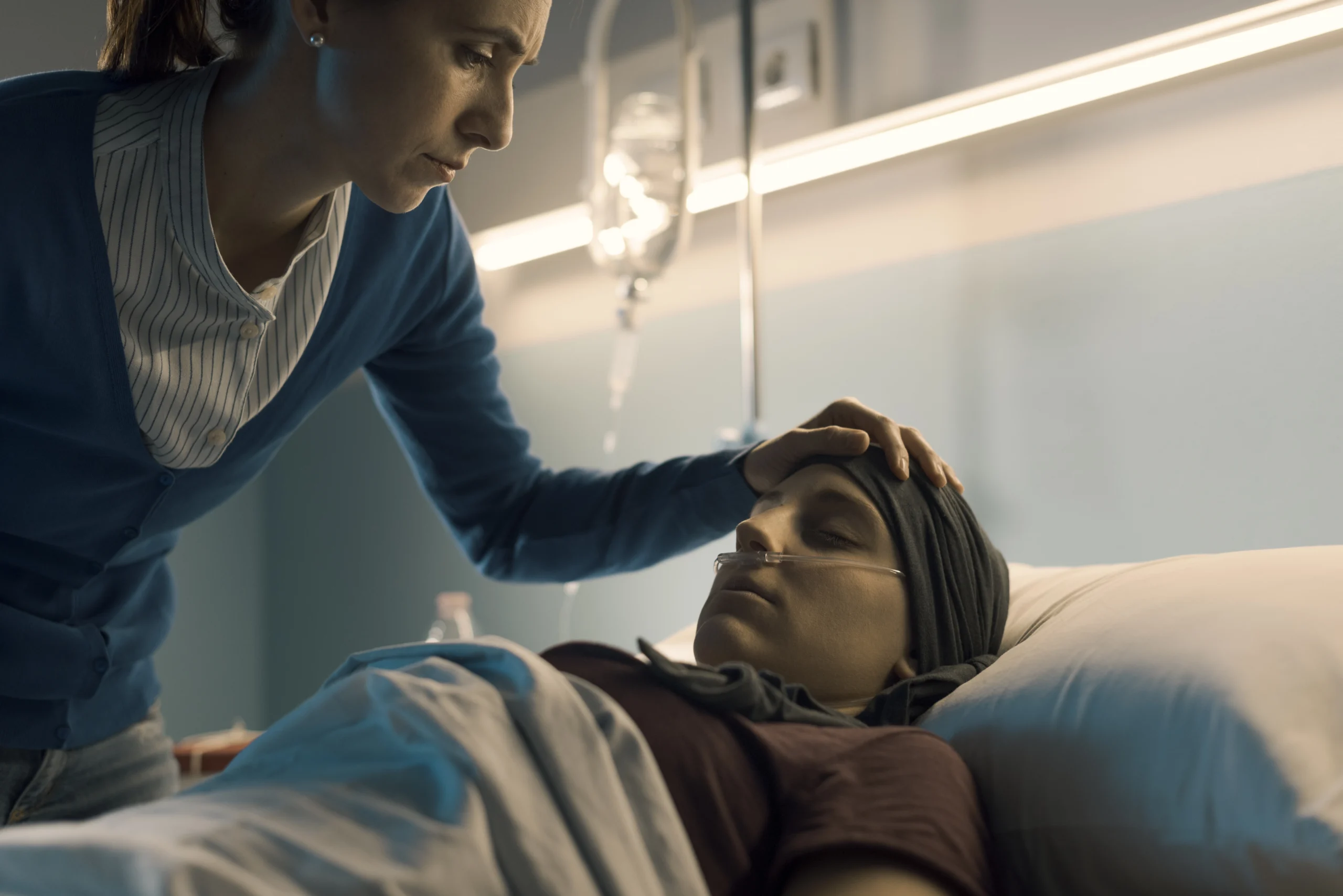 mother leaning over daughter in a hospital bed with her hand on her head.