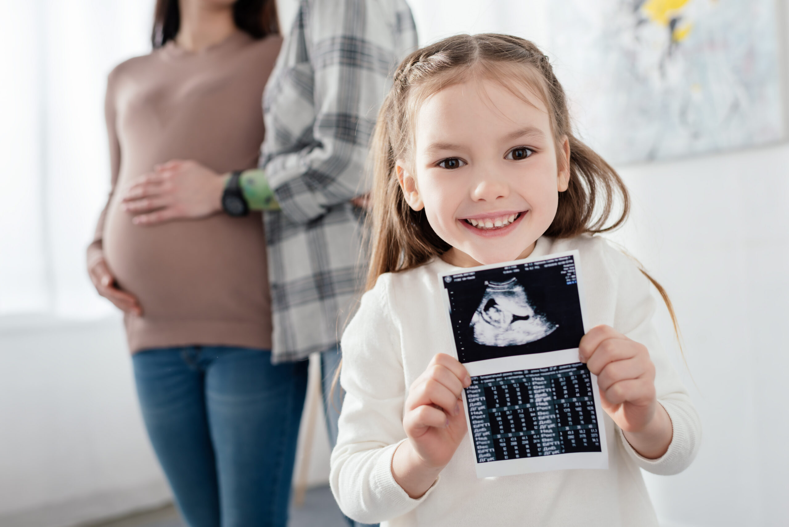 little girl holding a sonogram with parents in the background