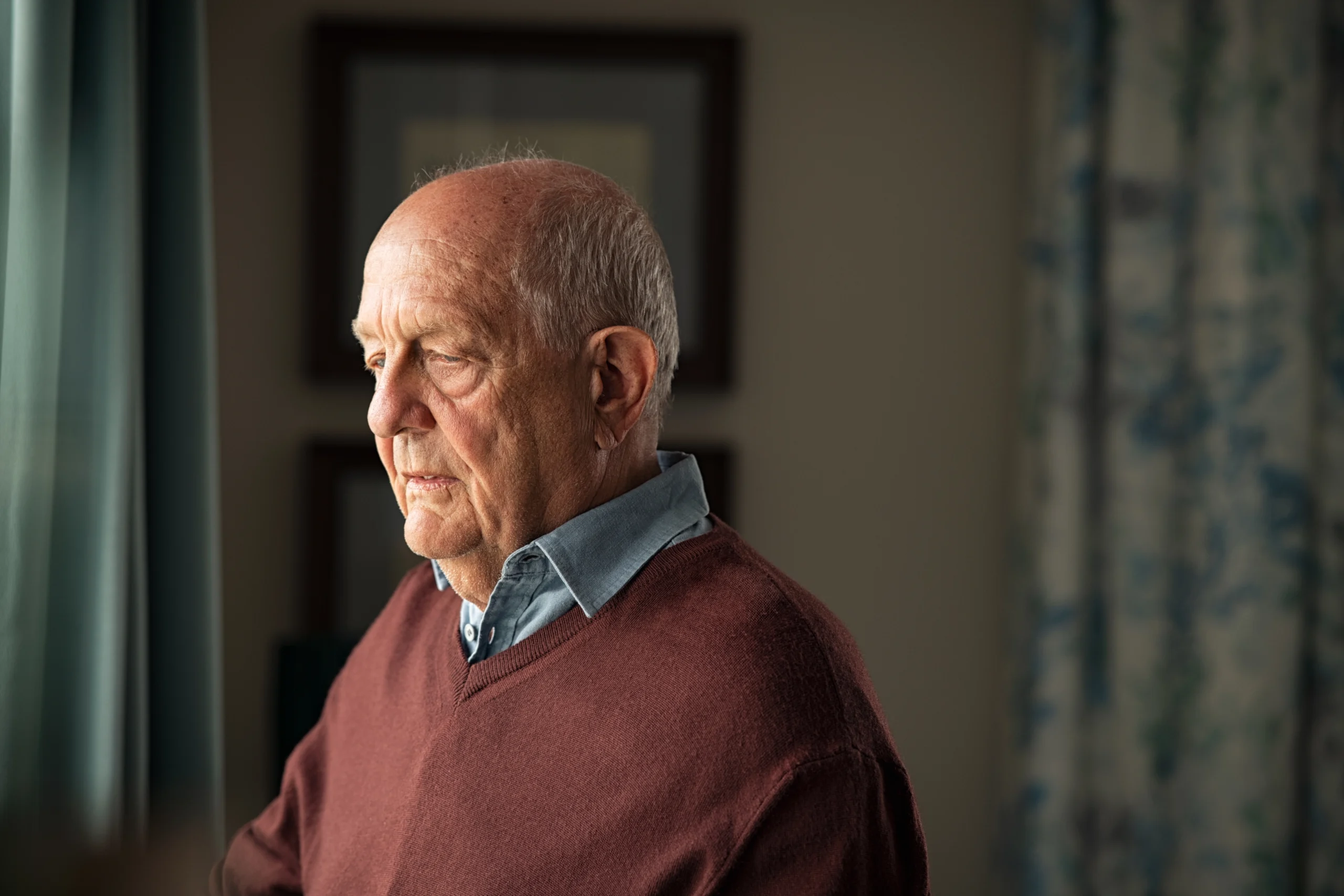 senior man looking sad and thoughtful in a room alone